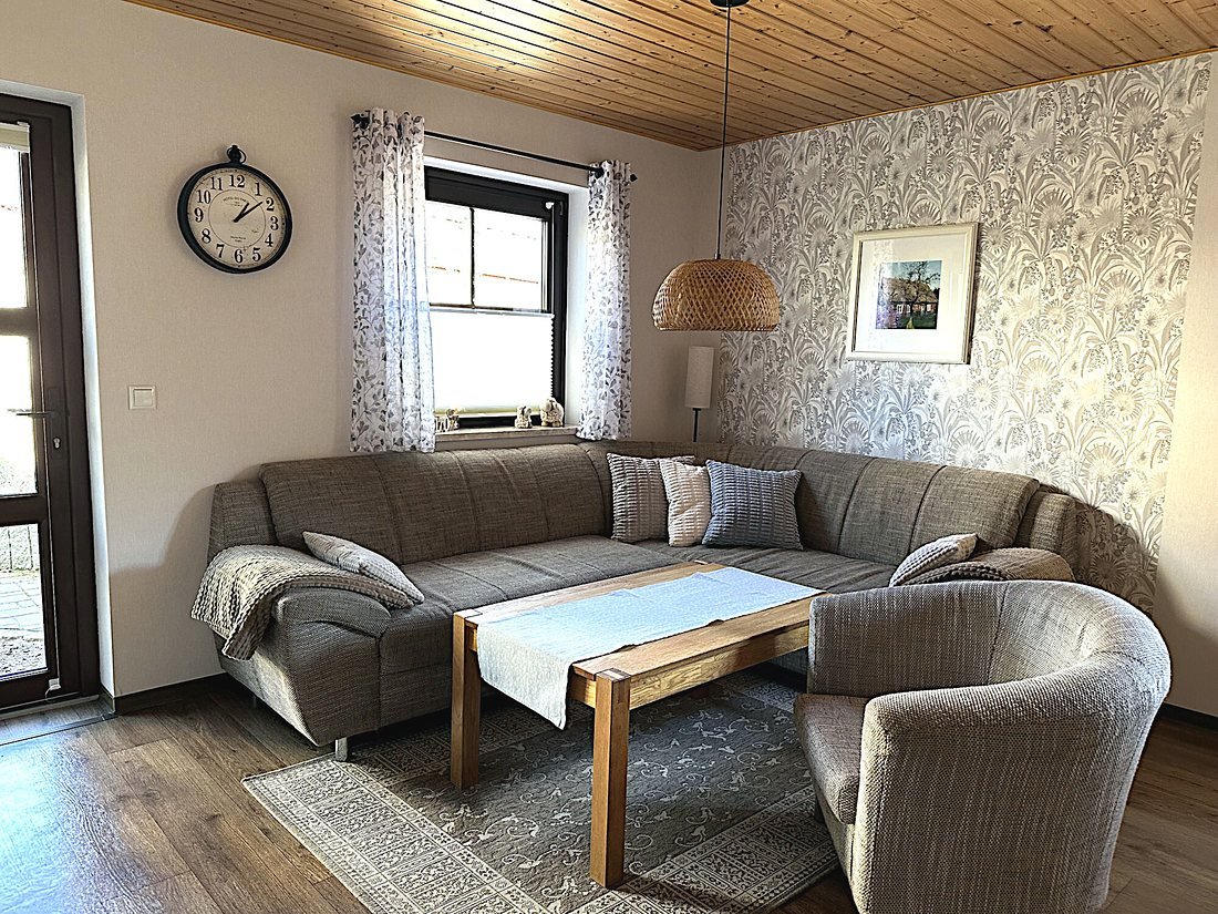 Wohnraum mit grauer Eckcouch, Holzdecke und Blick zum Fenster